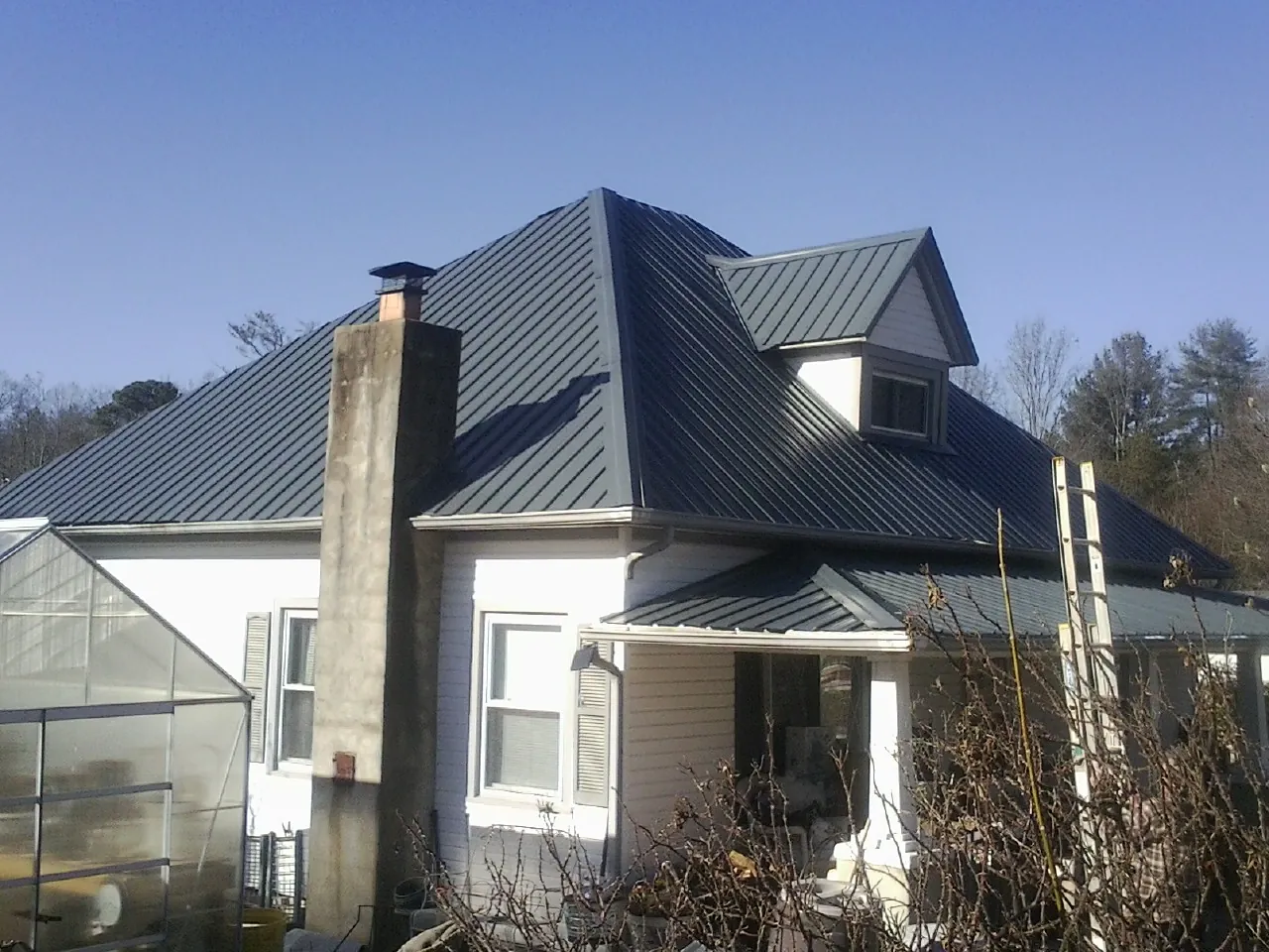 Dark blue standing seam metal roof on a white farmhouse with dormer — Slate & Tile Roof Repair by Roofing Brothers in Bourbon