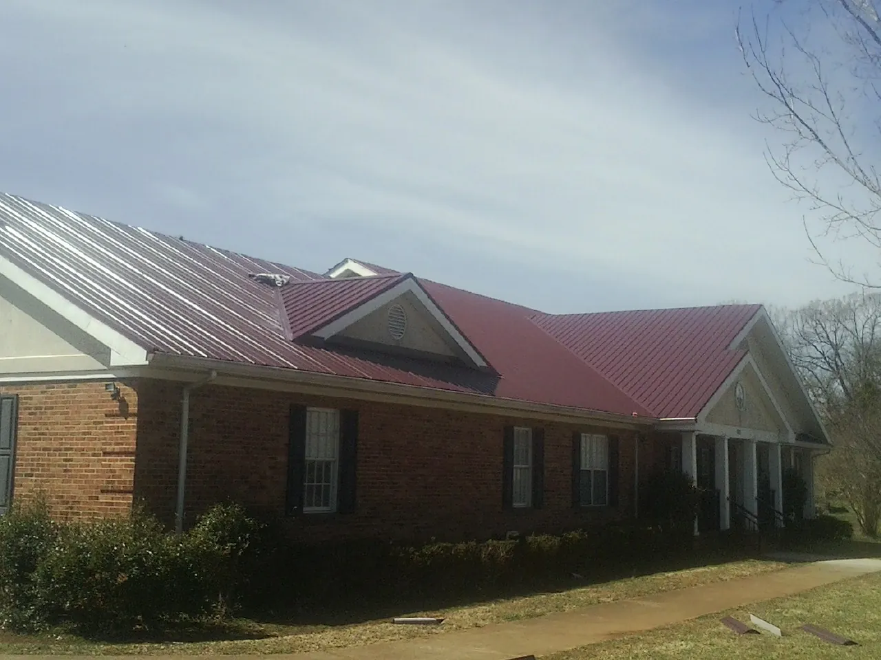 Red metal roof with gabled entries on a long brick building, from a Hail Damage Roof Repair job in Bourbon